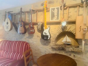 Et værelse med en pejs af sten, en rød stribet sofa og flere guitarer hængende på væggen.