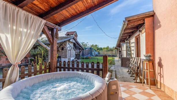 An outdoor hot tub area with a wooden pergola, a wooden fence, and a view of a traditional house in the background.
