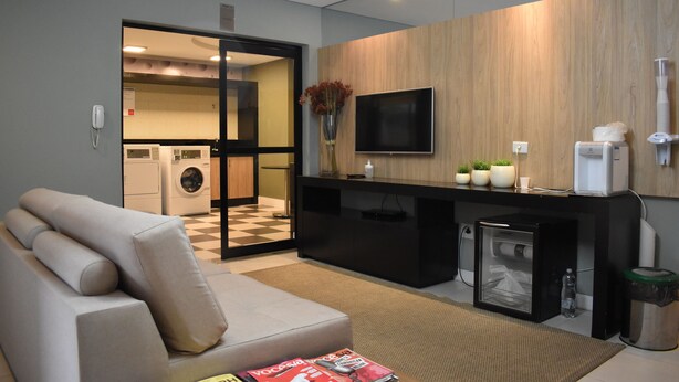 A modern living room with a sofa, a coffee machine, a TV, and a small refrigerator. - Studio near Botanical Garden (Cristo Rei Curitiba)