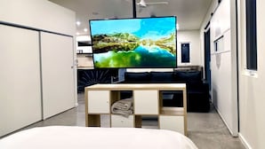 A modern hotel room with a large bed, a flat-screen TV on a wooden stand, and a wardrobe with multiple compartments. - Modern Accessible Studio Home w/ Yard  SolMod#3 (Tucson)