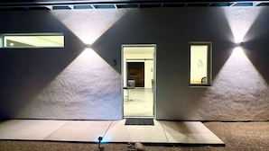 A modern building entrance with a door marked '5', a small window, and a wall-mounted light fixture. - Modern Accessible Studio Home w/ Yard  SolMod#3 (Tucson)