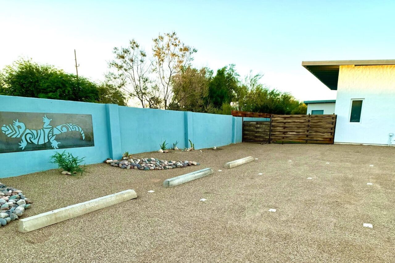 Un patio con una pared azul decorada con un mural, una zona de grava con rocas y plantas, y una valla de madera.