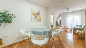 Un salon moderne avec une table ronde, des chaises blanches, un téléviseur et un canapé.