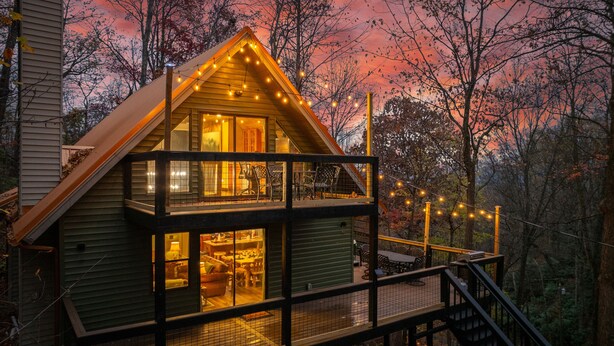 Eine zweistöckige Holzhütte mit einem Balkon, Lichterketten und Blick auf den umliegenden Wald.