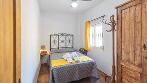 Un dormitorio con dos camas, un armario de madera, una ventana con cortinas amarillas y una mesita de noche con una lámpara.