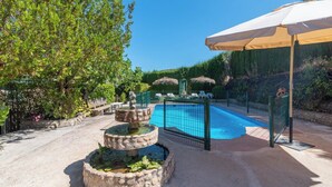 Una piscina con una fuente de piedra, rodeada por una cerca y una sombrilla.