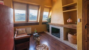 A cozy living room with a fireplace, wooden furniture, and large windows offering a mountain view.