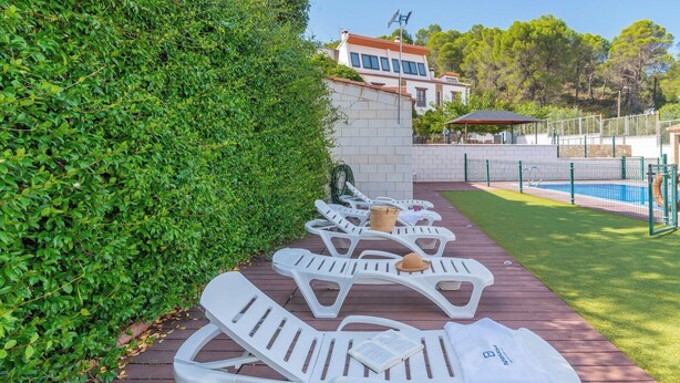 A poolside area with white lounge chairs, a wooden deck, and a hedge.
