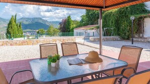An outdoor patio with a glass table, wicker chairs, a hat, and a potted plant.