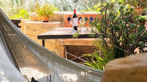 A hammock overlooking a patio area with a table, a bottle of wine, and potted plants.