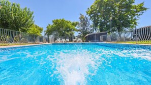 Une piscine à l’eau d’un bleu limpide, entourée d’une clôture et d’arbres.