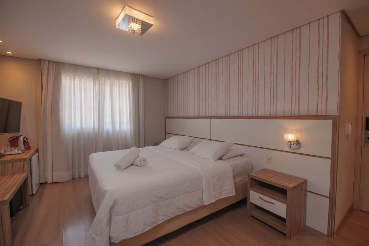 A hotel room with a large bed, bedside tables, a desk with a chair, and a television.