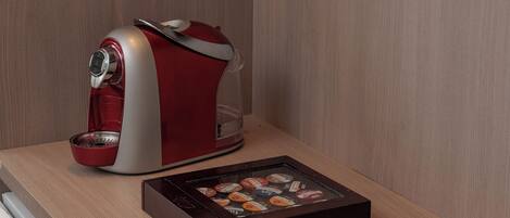 Una habitación de hotel moderna con un escritorio de madera, una cafetera roja y blanca, una bandeja con vasos y aderezos, y un televisor de pantalla plana.