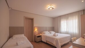 Hotellihuone, jossa on kaksi sänkyä, työpöytä, tuoli, yöpöytä lampun kanssa ja ikkuna, jossa on verhot.