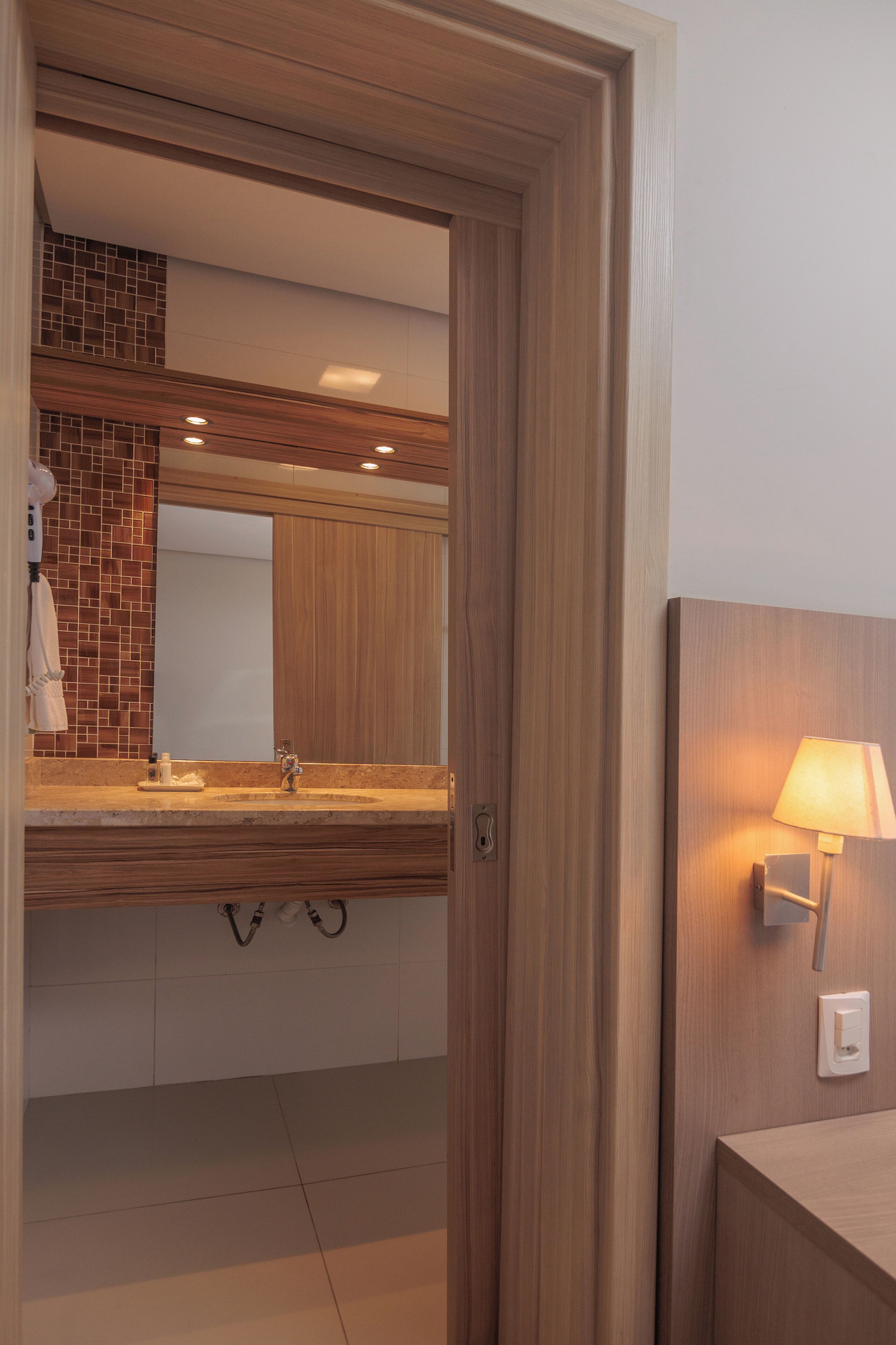 A modern bathroom with a wooden vanity, a large mirror, and a wall-mounted light fixture.