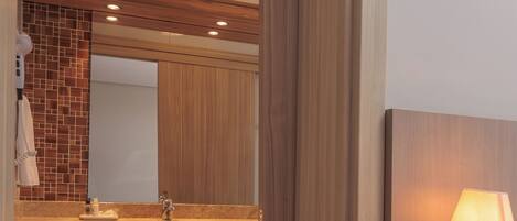 A modern bathroom with a wooden vanity, a large mirror, and a wall-mounted light fixture.