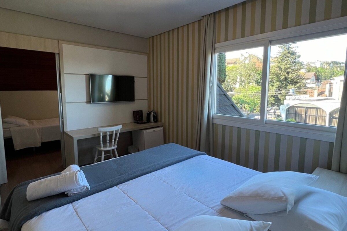 A hotel room with a large bed, a desk with a chair, a television, and a window with a view of the outside.