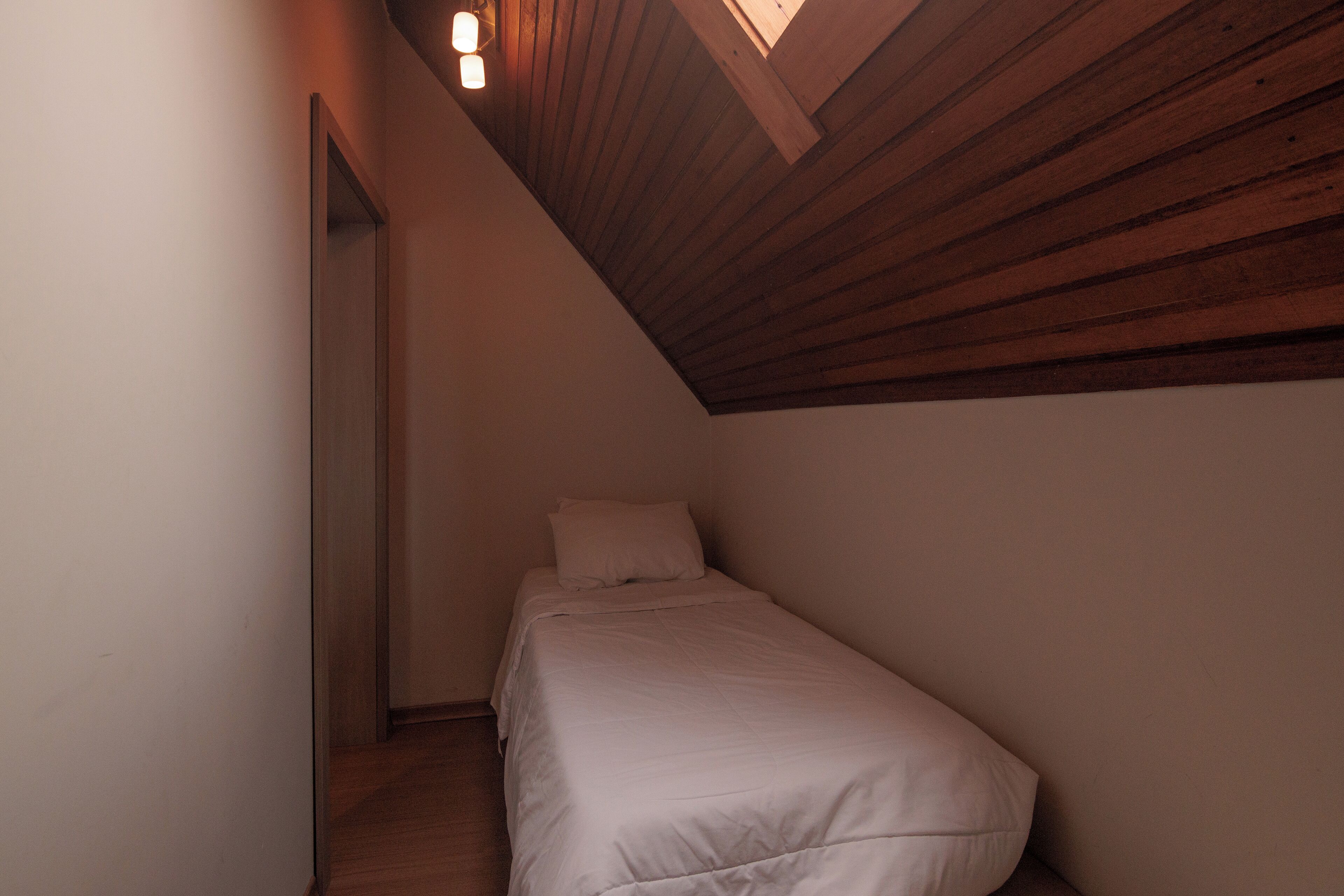 A small, narrow room with a sloped ceiling and a single bed.