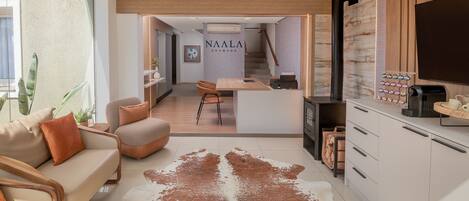 A modern living room with a sofa, a coffee table, and a large rug. There is a kitchen area with cabinets and a TV.
