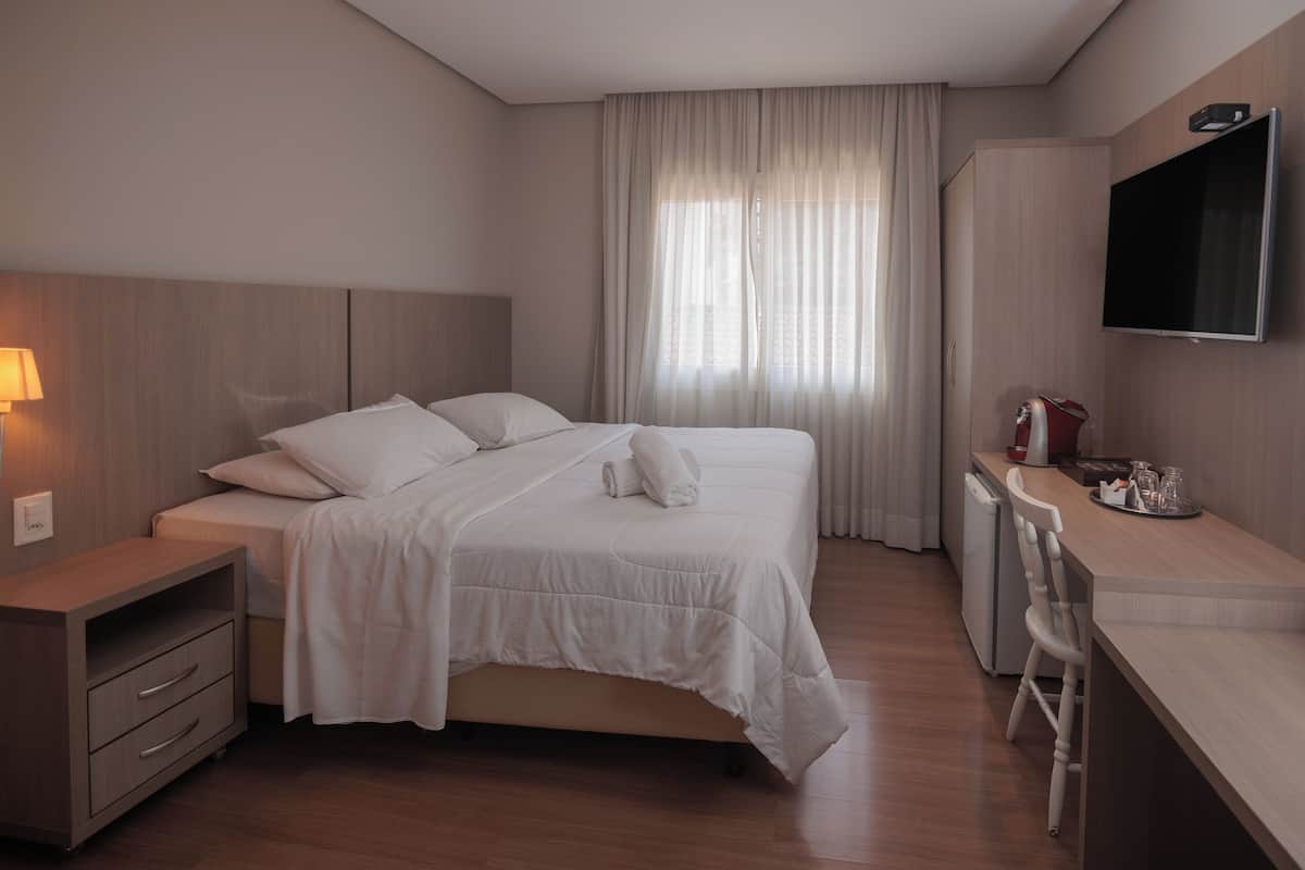 A hotel room with a bed, a desk, a TV, and a window with curtains.