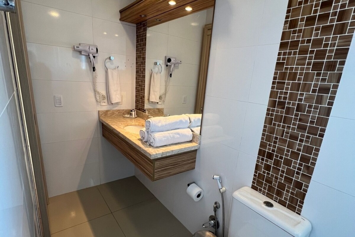 Un baño moderno con encimera de mármol, tocador de madera, un espejo grande y zona de ducha.