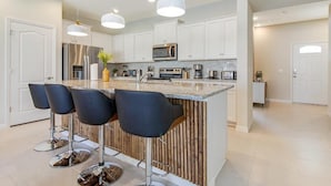 A modern kitchen with white cabinets, stainless steel appliances, and a central island with bar stools. - Spacious 5-bedroom Town home Pvt Pool, BBQ & Free Water Park Access Near Disney (Kissimmee)