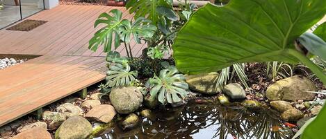 A serene garden with a koi pond, a Buddha statue, and lush greenery.