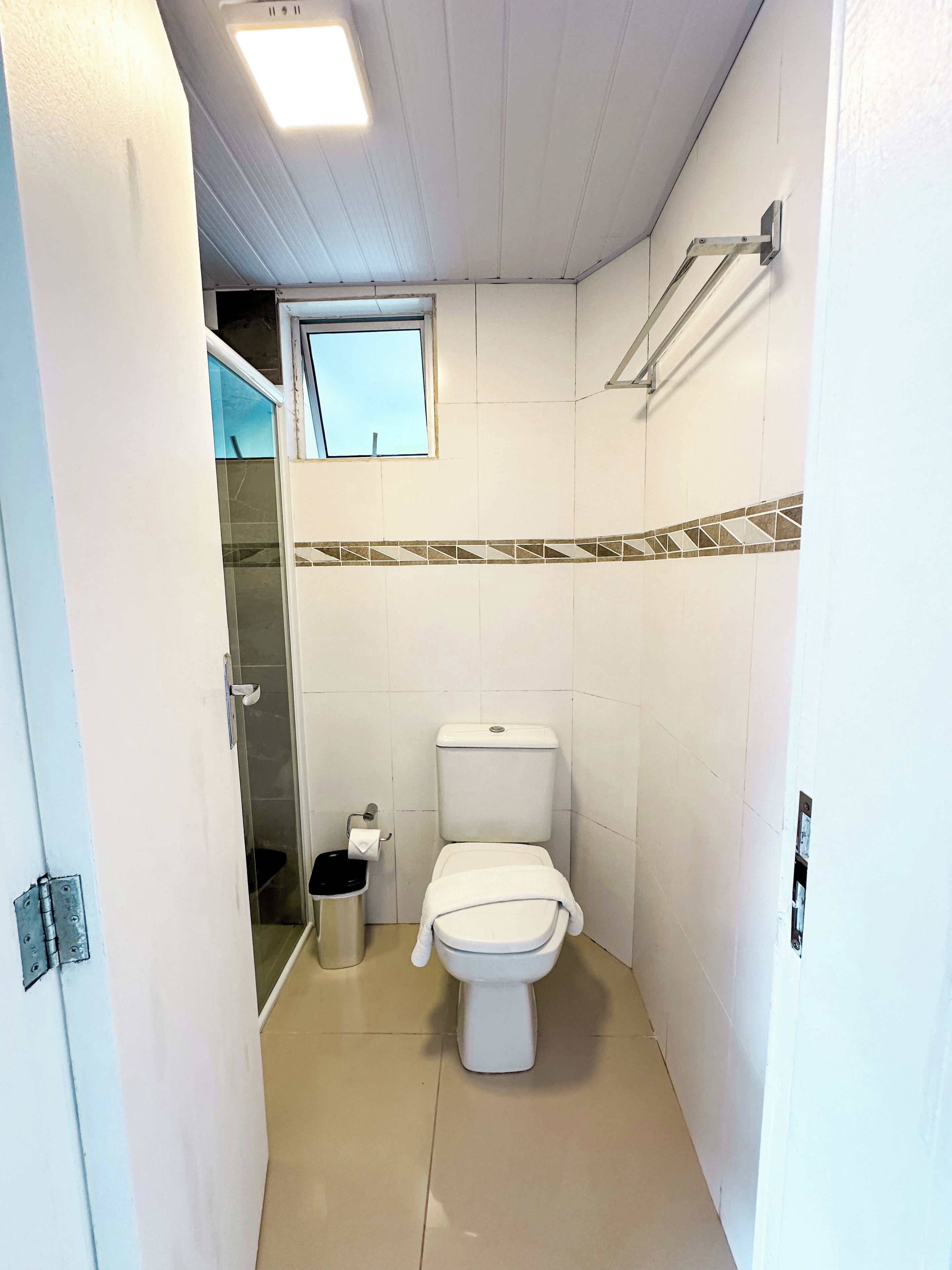 A small, compact bathroom with a toilet, a trash bin, and a window.