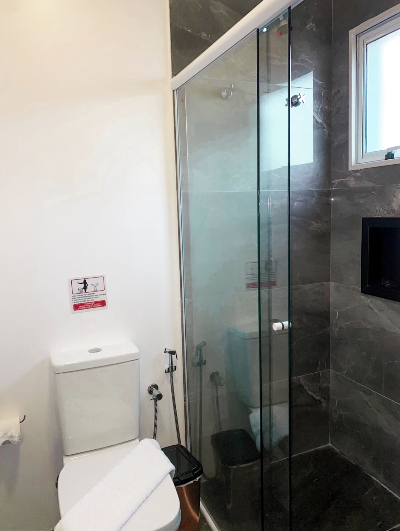 A modern bathroom with a glass-enclosed shower, a white toilet, and a black trash bin.