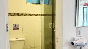 Un baño con inodoro, cabina de ducha de vidrio y un secador de pelo montado en la pared.