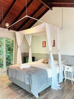 Camera da letto con un letto a baldacchino, un comodino e vista sul verde attraverso un'ampia finestra.