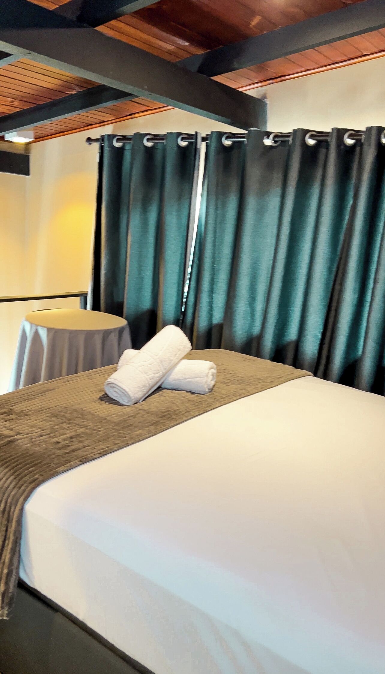 A hotel room with a neatly made bed, a round table, and a curtain.