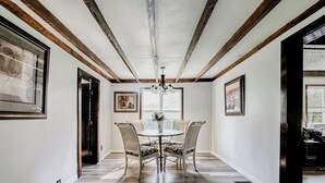 A hallway with a dining area featuring a round table and four chairs, wooden beams on the ceiling, and framed artwork on the walls. - Crooked Little Farmhouse! Spacious 2-bed on 2+ acres - Romeo, MI (Bruce Township)