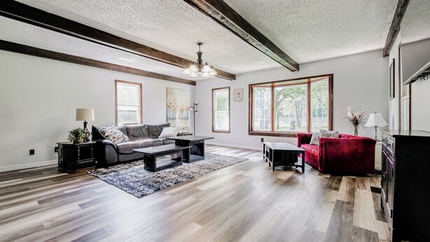 A spacious living room with hardwood flooring, a dark sofa, a red couch, and a large window providing natural light. - Crooked Little Farmhouse! Spacious 2-bed on 2+ acres - Romeo, MI (Bruce Township)