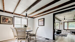 A dining area with a round table, four chairs, and a vase of flowers. There are framed pictures on the walls and a ceiling with exposed beams. - Crooked Little Farmhouse! Spacious 2-bed on 2+ acres - Romeo, MI (Bruce Township)