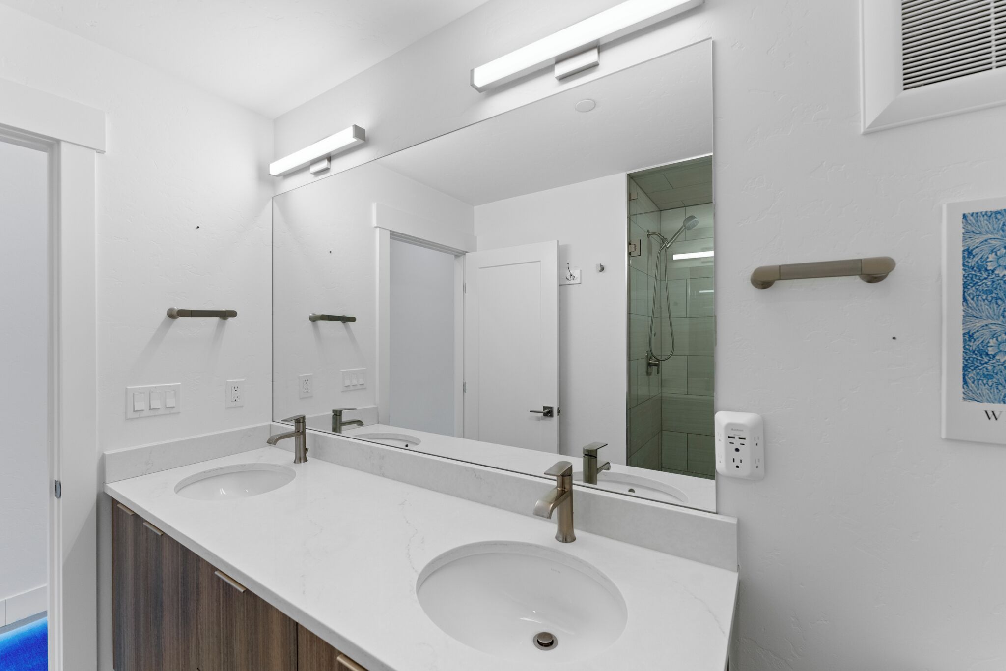 A modern bathroom with two sinks, a large mirror, and a shower visible through a glass door.