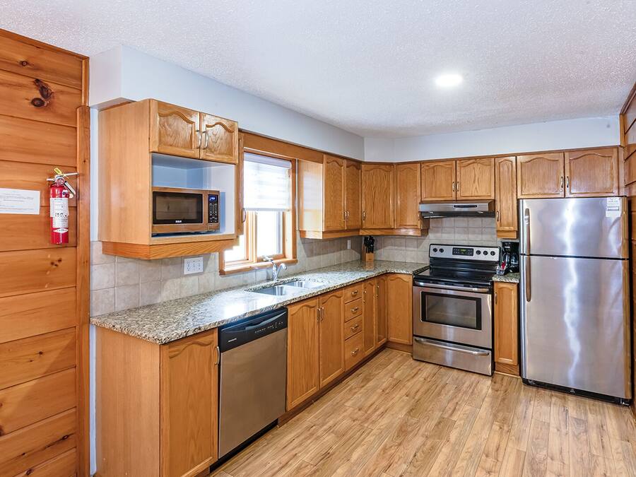 Una cocina compacta con armarios de madera, un refrigerador de acero inoxidable, un microondas, un lavavajillas y una estufa.