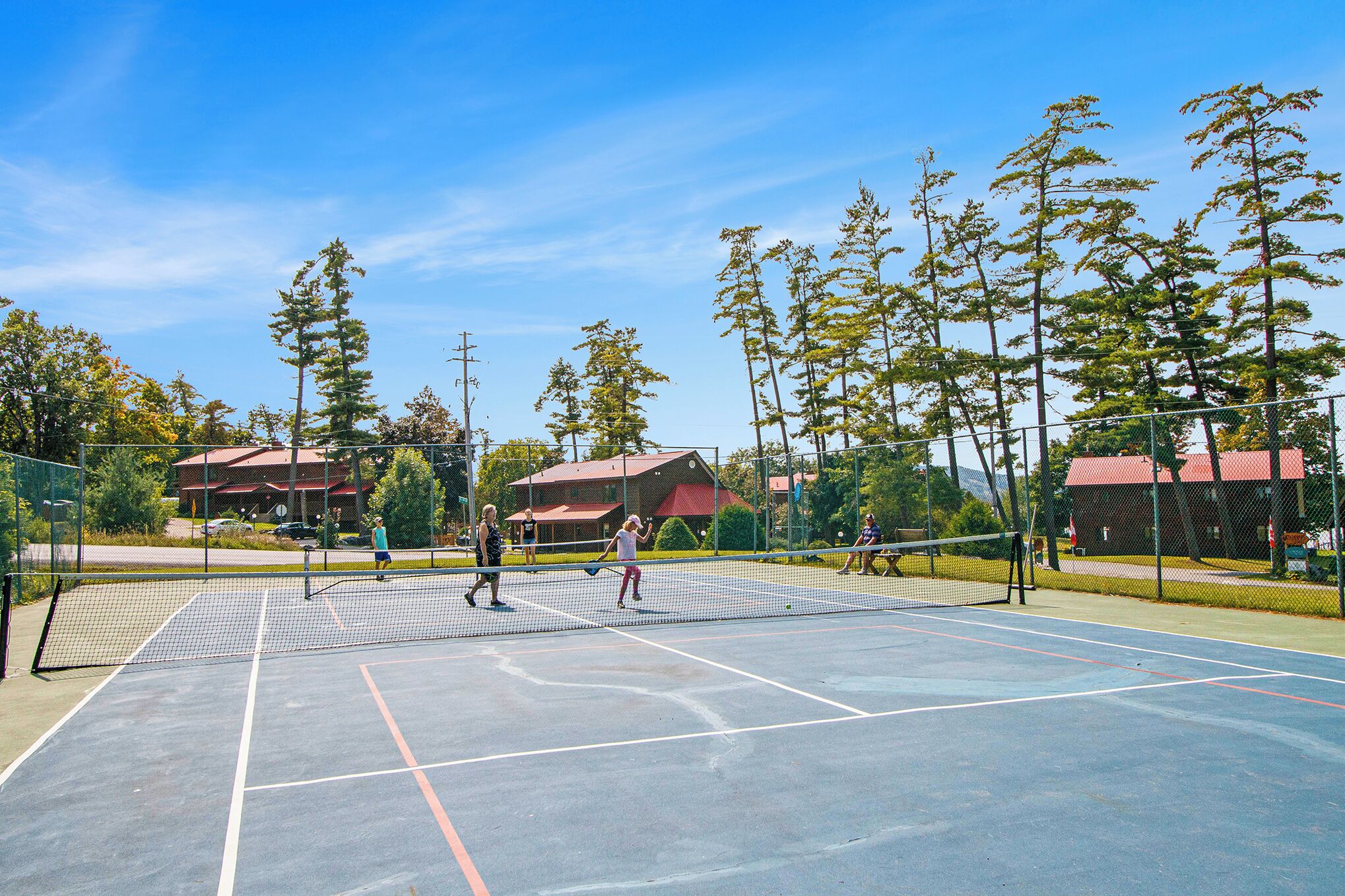 An outdoor tennis court with a net, surrounded by trees and buildings.