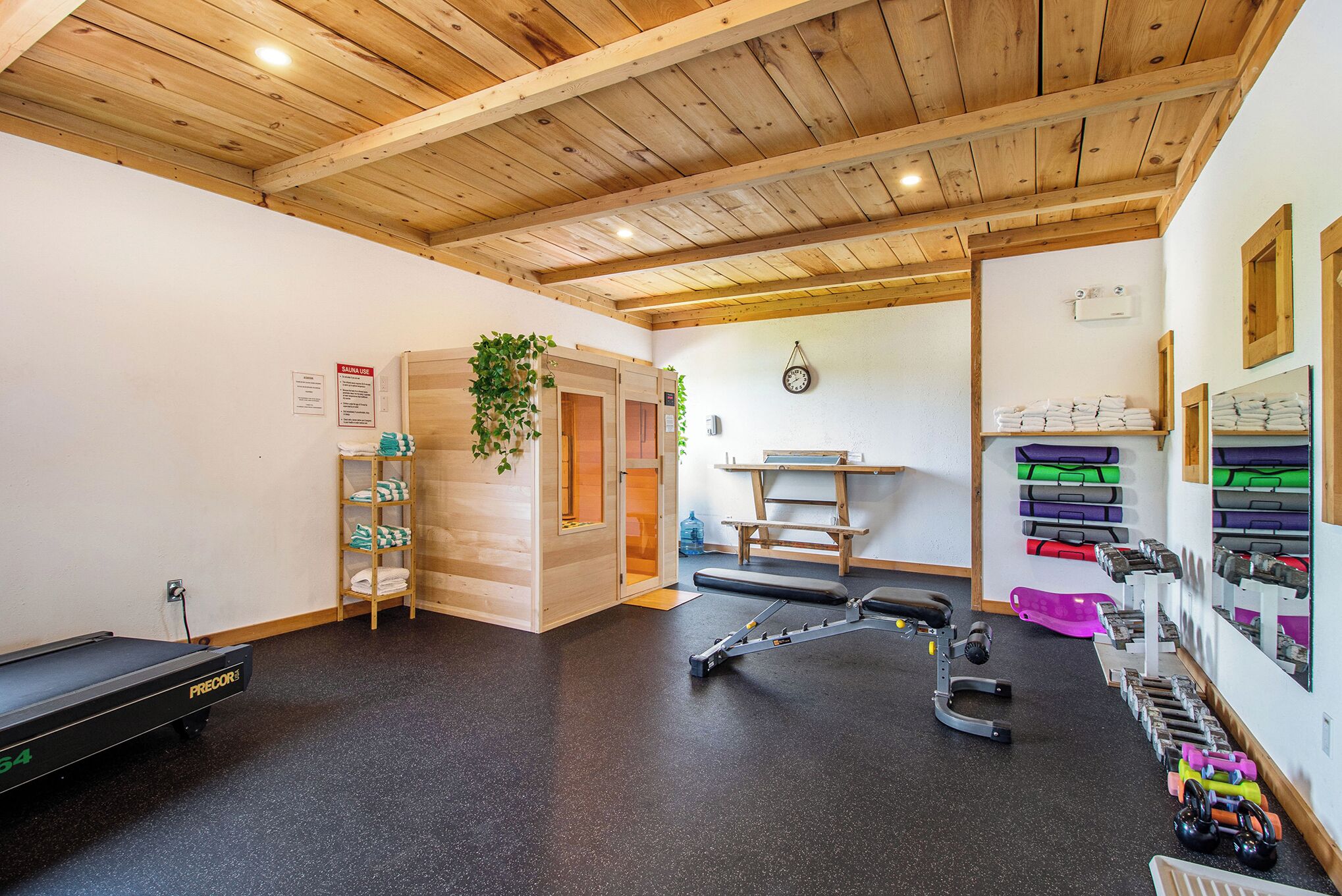 A gym with wooden beams, exercise equipment, and a sauna.