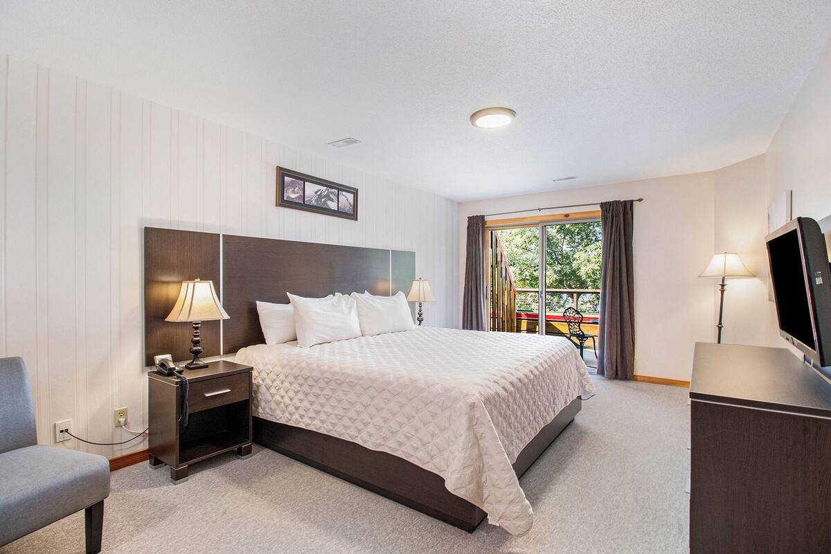 Una habitación de hotel con cama, mesitas de noche, televisor y ventana con cortinas.