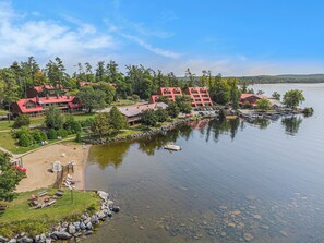 A lakeside hotel with multiple red-roofed buildings, a sandy beach area with lounge chairs, and a dock with boats. - Calabogie Lodge (Calabogie)