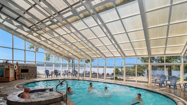 An indoor swimming pool with a view of a lake, surrounded by stone flooring and metal railings. - Calabogie Lodge (Calabogie)