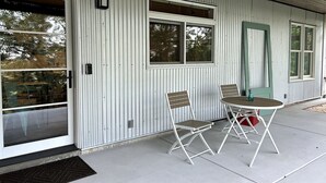 A metal building with a sliding glass door, a small porch with a table and two chairs, and a green door.