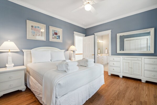 A bedroom with a large bed, white nightstands, a dresser, and a mirror.