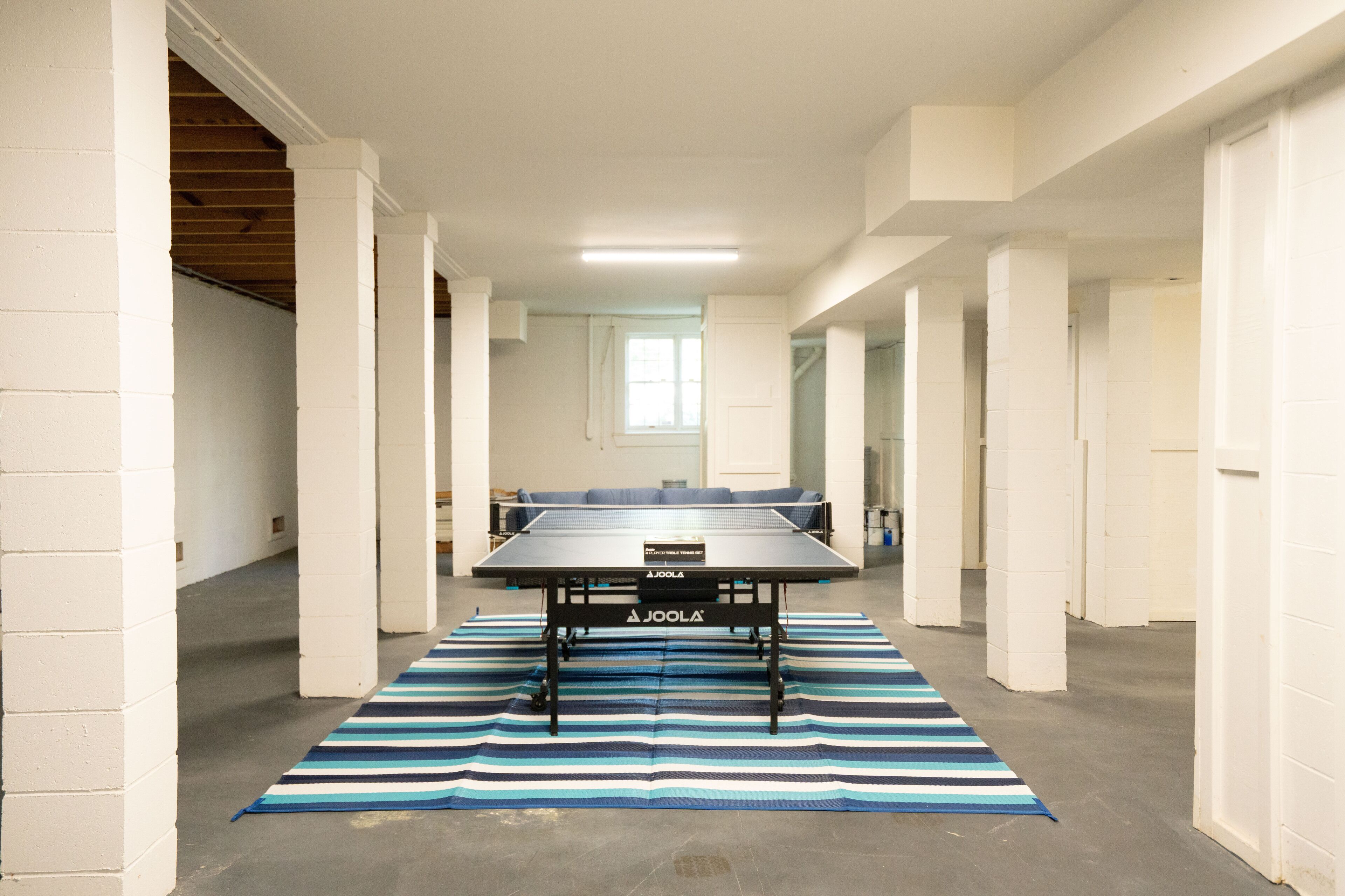 A spacious room with a ping pong table, white walls, and a striped rug.