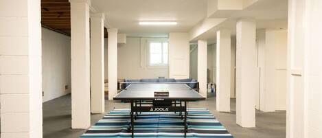 A spacious room with a ping pong table, white walls, and a striped rug.
