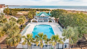 A beachfront property with a swimming pool, palm trees, and a view of the ocean.