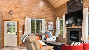 A cozy living room with a sofa, red armchairs, a fireplace, and a large window with curtains.