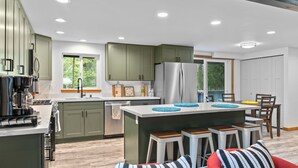 A modern kitchen with green cabinets, a stainless steel refrigerator, and a central island with stools.