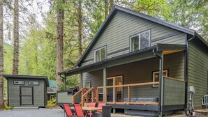 A cabin with a covered porch, a dining area with outdoor seating, and a small shed in a forested area.